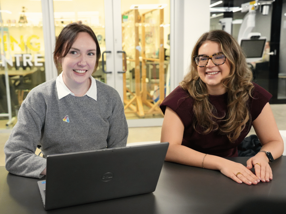 Two members of the innovation team sitting together at a table with a laptop in an open innovation space.