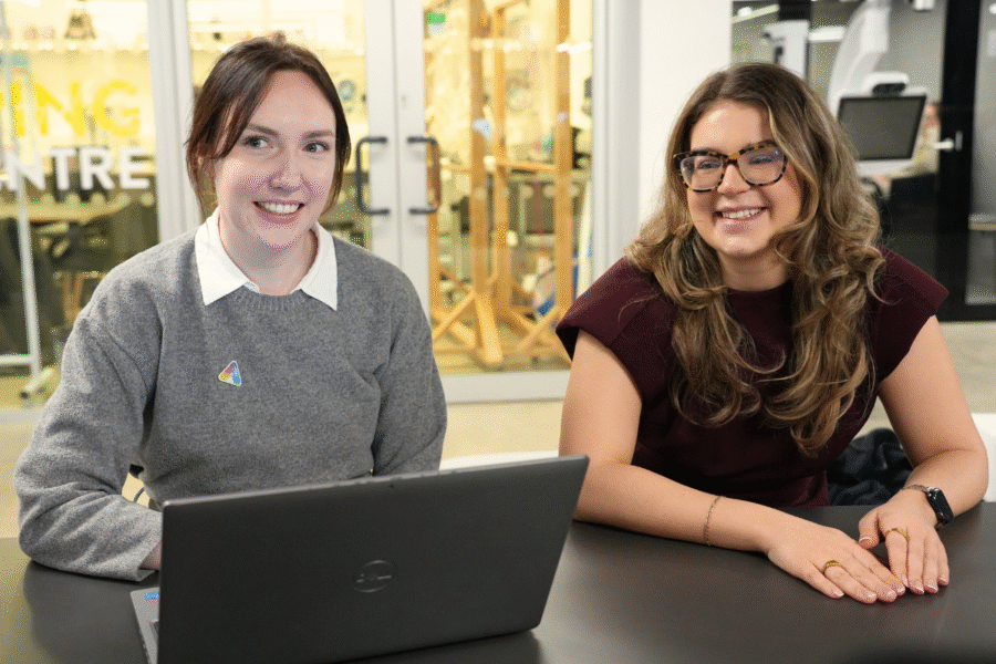 Two members of the innovation team sitting together at a table with a laptop in an open innovation space.